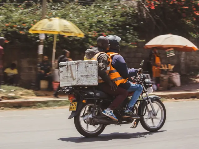A motorcycle rider carrying a delivery box through a Nairobi street