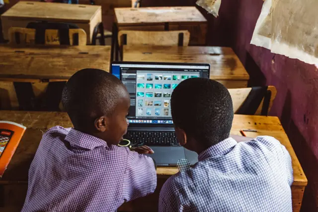 Two schoolboys in uniform working on a laptop in a classroom